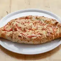 Khachapuri géorgien allongé, garni de fromage fondu et de tranches de tomate, servi sur une assiette blanche ovale.