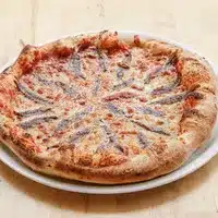 Pizza napolitaine cuite au four, garnie de sauce tomate, fromage et disposée artistiquement de filets d'anchois.