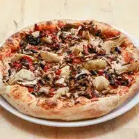 Pizza végétarienne artisanale, bien cuite, garnie de champignons, d'artichauts et de poivrons rouges sur une croûte dorée, servie sur une assiette blanche.