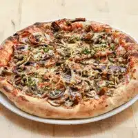 Pizza rustique aux champignons et herbes vertes, bien cuite avec une croûte dorée et boursouflée, présentée sur une assiette blanche.