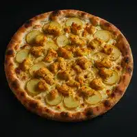 Pizza garnie de morceaux de poulet doré et de fines tranches de pommes de terre sur une base de fromage crémeux, vue de dessus sur fond noir.