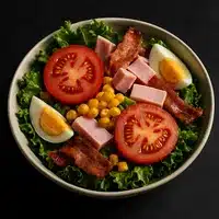 Salade composée garnie de laitue, tranches de tomates, dés de jambon, morceaux de bacon croustillants, maïs et œufs durs coupés en deux.