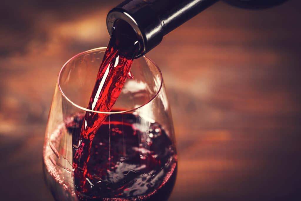 Gros plan d'un vin rouge riche et foncé versé d'une bouteille dans un verre à vin, créant des remous intenses.